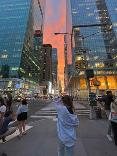 a woman taking a photo in the middle of a busy city street at sunset with tall buildings