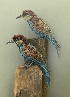 two wire birds sitting on top of a piece of wood with string wrapped around them