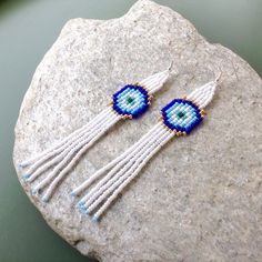 Lucky Eye Tassel Earrings,Blue Eye Fringe Earrings,Minimalist Boho,Protection Jewelry,Dangle Earrings,Long Seed Beaded Earrings Dimensions: Width- 0.8 inches /2cm Length (incl. ear wires)- 4.7 inches /12 cm These adorable earrings are a fun and lovely accessory, perfect for a gift or just for no reason! They are made from OUR ORIGINAL pattern, made from high quality glass beads, very lightweight. *Please note that real colors may slightly differ from their appearance on your display! Ready to Sh White Tassel Earrings With Latkans As Gift, White Tassel Earrings With Latkans For Gift, Gift Long Drop Tassel Earrings, Handmade White Dangle Plug Earrings, White Drop Earrings With Latkans, White Dangle Jewelry With Latkans, White Latkans Drop Earrings, White Latkan Drop Earrings, Coachella Jewelry