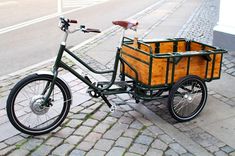 a bicycle with a wooden basket is parked on the sidewalk next to a brick road