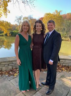 three people standing next to each other in front of a lake