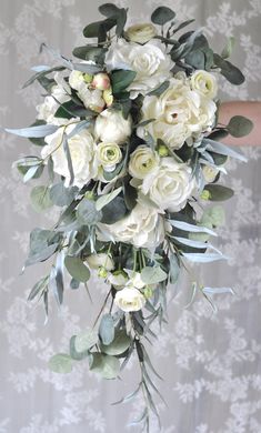 a bridal bouquet with white flowers and greenery is held by someone's hand