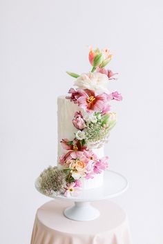 a white cake with pink and orange flowers on it sitting on top of a table