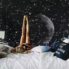 a woman laying on top of a bed in front of a wall with stars and the moon