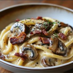 pasta with mushrooms and bacon in a white bowl on a wooden table, ready to be eaten