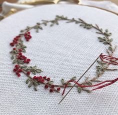 a close up of a piece of embroidery on a white cloth with red flowers and leaves