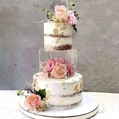 a three tiered cake with pink flowers on the top and gold leaf decoration around it