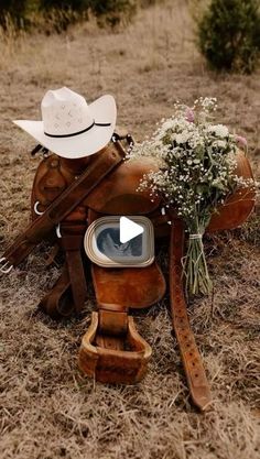 a cowboy hat sitting on top of a brown saddle with flowers in the back ground