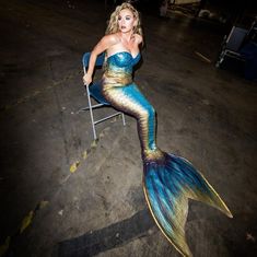 a woman sitting in a chair with a mermaid tail on her head and body painted blue, gold and green