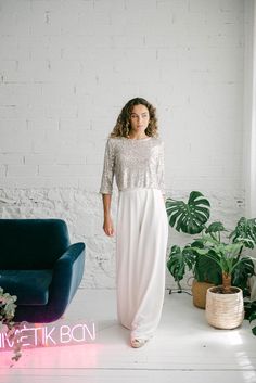 a woman standing in front of a white brick wall wearing a long dress with sequins on it