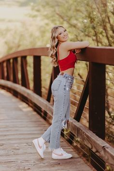 a beautiful young woman standing on top of a wooden bridge