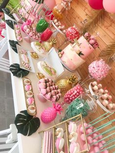 a table topped with lots of pink and green desserts next to palm leaves on top of wooden flooring