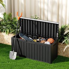 an outdoor storage box with shovels, balls and other items in it on the grass