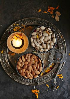 three bowls filled with nuts on top of a metal tray next to a lit candle