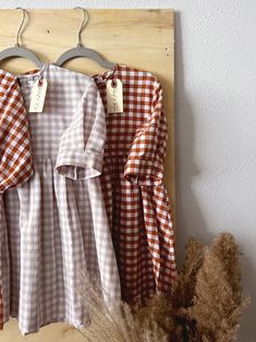 an orange and white gingham dress hanging on a wooden hanger next to dried grass