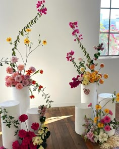 three white vases filled with flowers on top of a wooden floor