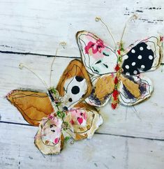 three butterflies with different designs on them sitting on a white wooden surface, one has black spots and the other has pink flowers