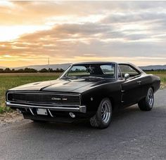 an old black muscle car parked on the side of the road in front of a field