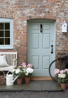 a bicycle parked next to a brick building with flowers in front of the door and two chairs