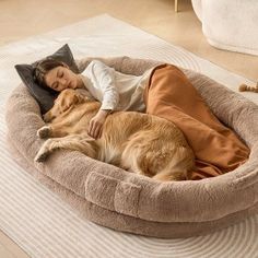 a woman laying on top of a dog bed next to a large golden retriever