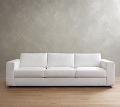 a white couch sitting on top of a hard wood floor next to a gray wall