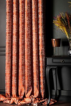 an orange curtain is hanging in front of a black table with a vase on it