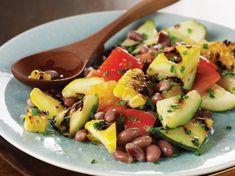 a salad with beans, cucumbers and other vegetables on a plate next to a wooden spoon