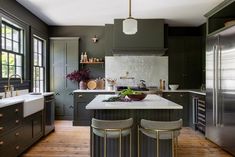 a large kitchen with green cabinets and white counter tops, along with two stools in front of the island