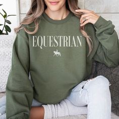 The perfect equestrian sweatshirt for a stylish horse lover! Customize it with a symbol that reflects your riding life. Made from a gentle, midweight cotton blend, this sweatshirt is your go-to for easy layering on crisp days or a stand-alone choice for ultimate comfort. Packed with both style and coziness, we're convinced this sweatshirt checks all the boxes for the ideal pick for any rider. At the heart of our creations lies a commitment to quality and a touch of nostalgia. We bring our designs to life through a premium direct-to-garment (DTG) printing process, where fabric-grade ink embraces each garment, merging gracefully with the fibers. This isn't just about style; it's about creating a warmth reminiscent of vintage charm. Our prints, crafted with care, offer a cozy and inviting fee Riding Shirts Equestrian, Horse Shirts For Women, Equestrian Sweatshirts, Horse Riding Shirt, Blank Sweatshirts, Horse Riding Shirts Long Sleeve, Horse Hoodies, Equestrian Gifts, Horse Owner