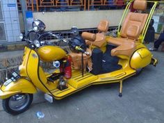 a yellow motor scooter with two seats on the front and side, parked in front of a building