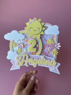 someone is holding up a greeting card with the number two on it and flowers in the background