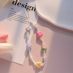 a necklace with flowers and pearls on it sitting next to an open book that says design