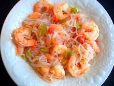 a white plate topped with pasta and shrimp next to a fork on a black table