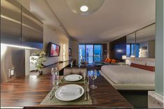 a dining table with place settings in front of a bed and large window overlooking the city