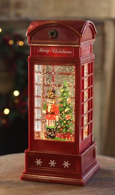 a red phone booth sitting on top of a wooden table next to a christmas tree