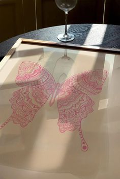 a wine glass sitting on top of a table next to a butterfly drawn on paper