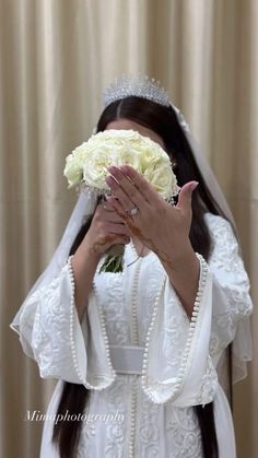 a woman wearing a wedding dress holding a bouquet of flowers in front of her face