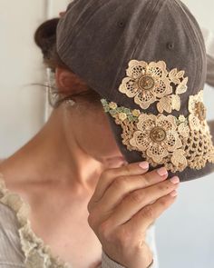 a woman wearing a brown hat with flowers on it's brim and holding her face up to the side