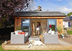 a dog laying on the ground in front of a small wooden building with patio furniture