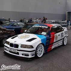 a bmw race car parked next to other cars in a parking lot with people standing around