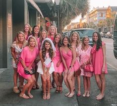 a group of women standing next to each other in pink dresses on the sidewalk near a building