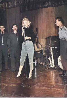 a woman singing into a microphone while standing next to two men in suits and ties