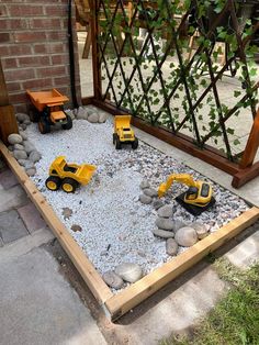 toy construction vehicles sitting on gravel in front of a fence