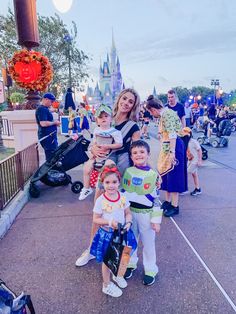 a woman and two children standing in front of a castle at disney world with other people