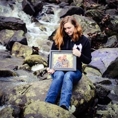 a woman sitting on rocks holding a framed photo