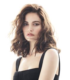 a woman with long hair wearing a black dress and posing for a photo in front of a white background