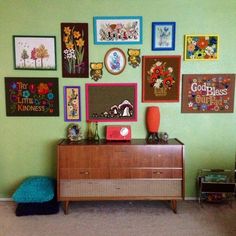 a green wall with many pictures on it and a dresser in the foreground is a blue bean bag