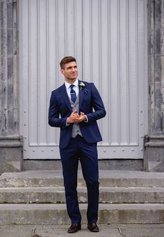 a man in a blue suit and tie standing on steps with his hands in his pockets