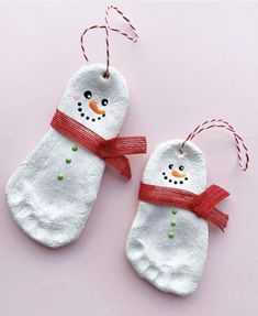 two snowman mittens hanging from string on pink surface