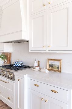 a kitchen with white cabinets and gold trim on the stove top, along with an oven hood